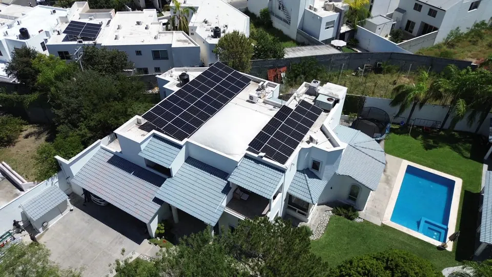 Vista aérea de una casa con paneles solares en la azotea y alberca en el jardín