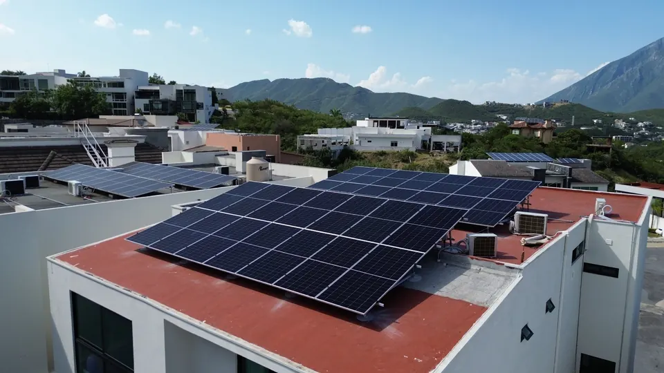 Casa con techo rojo y paneles solares en la azotea, con montañas al fondo